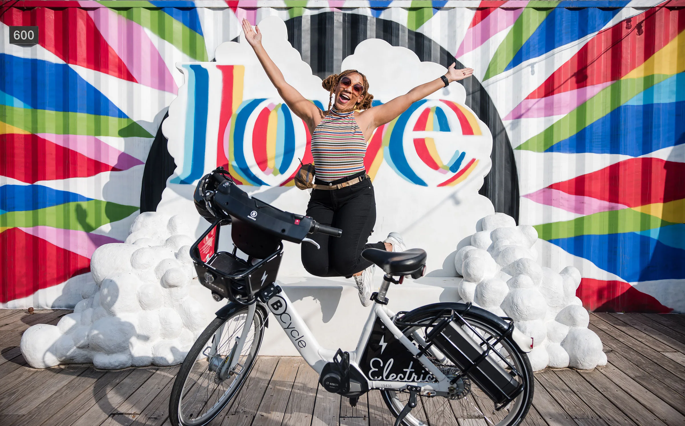 Photo of woman jumping with joy in front of a mural behind a bike share bicycle