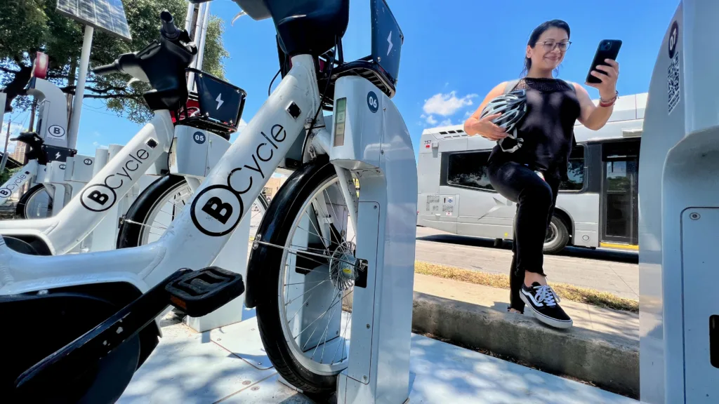 Photo of woman getting off a public bus checking her BCycle app walking up to a bike share docking station.