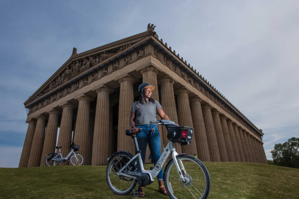 Photo of woman standing with a bike share bicycle in front of the Nashville Parthenon. 