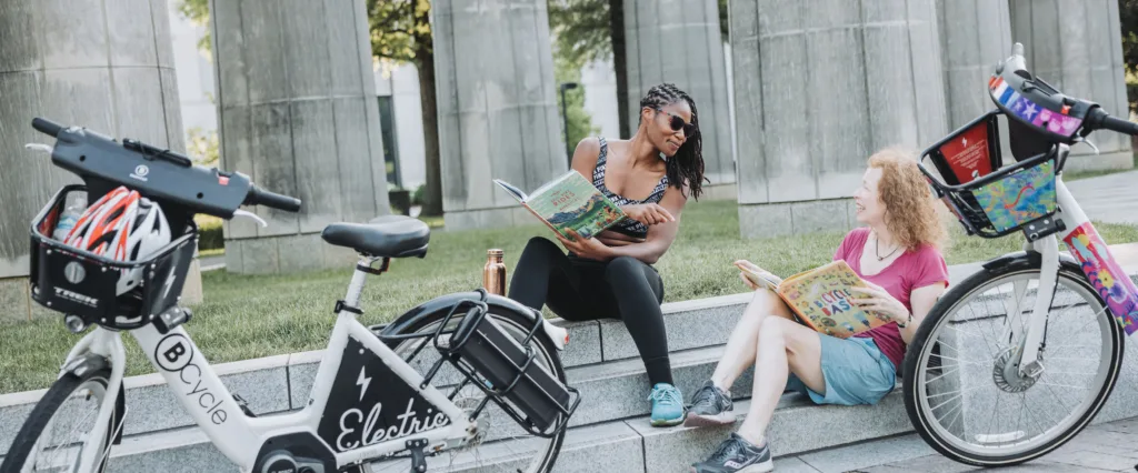 photo of two women reading books while riding bike share bicycles